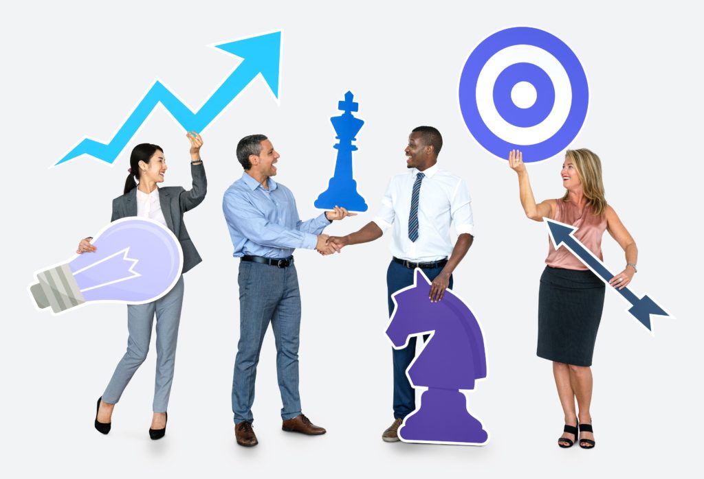 Four people in business attire holding blue and purple cartoon images of a target, chess pieces, and arrows.