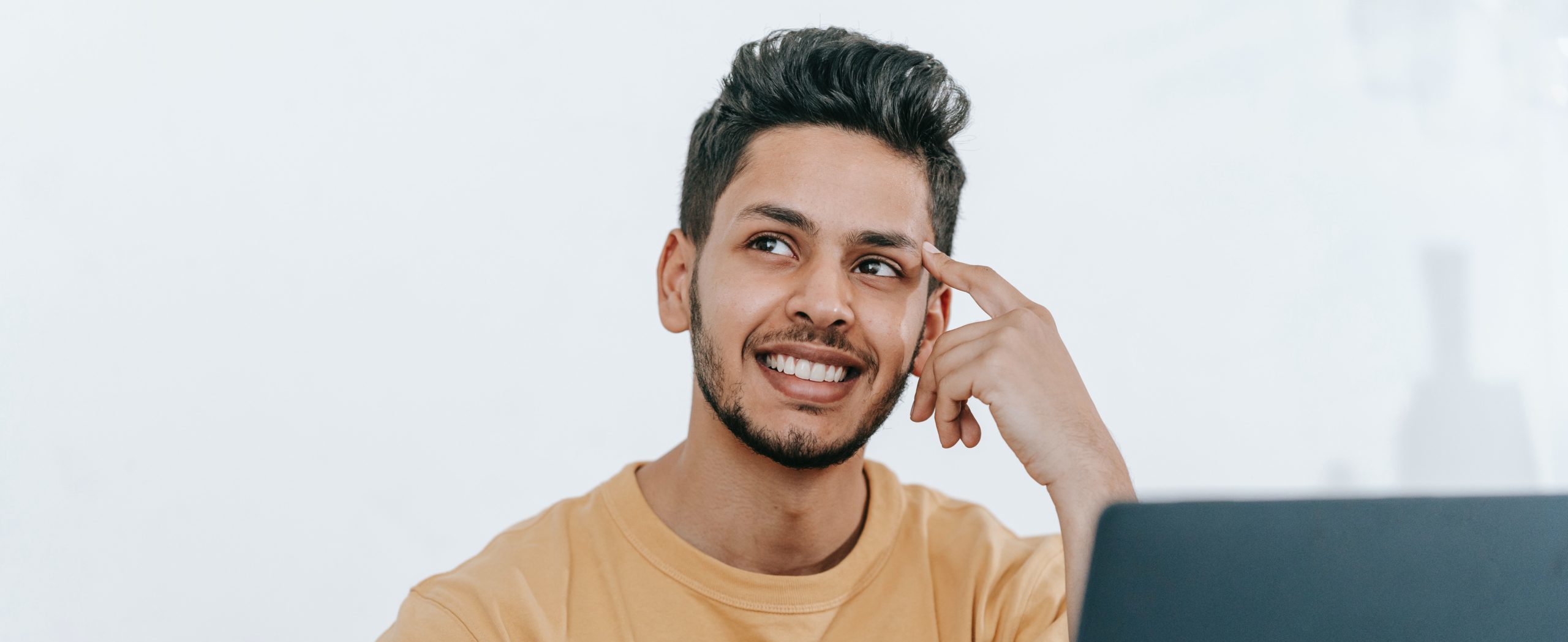 A young hispanic man sits infront of a computer thinking of an idea